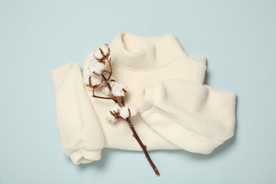 Photo of Warm sweater and cotton flowers on light blue background, flat lay. Autumn season