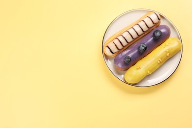 Photo of Delicious eclairs covered with glaze on yellow background, top view. Space for text