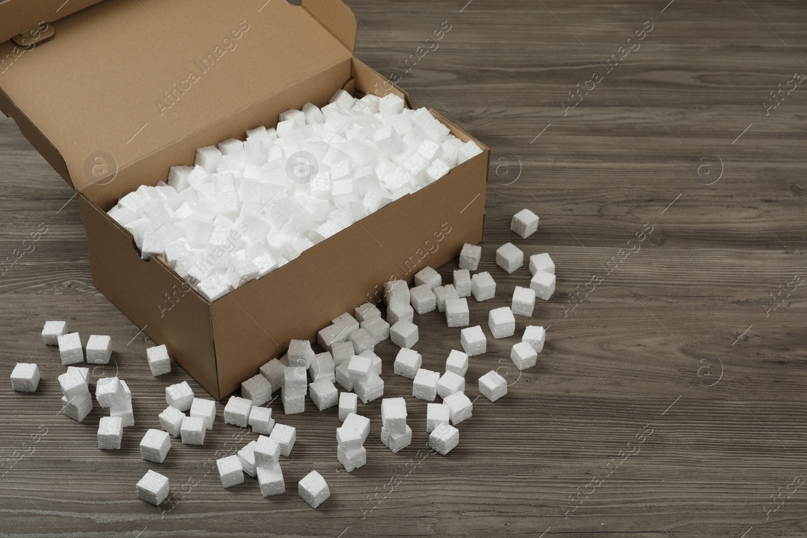 Photo of Cardboard box and styrofoam cubes on wooden floor. Space for text
