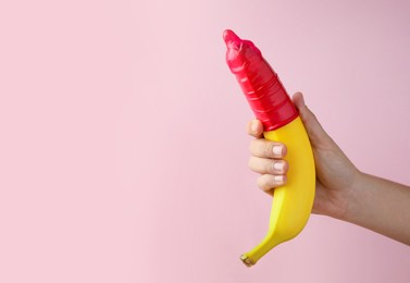 Photo of Woman holding banana in condom on pink background, closeup and space for text. Safe sex concept