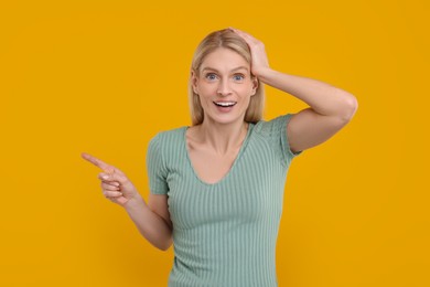 Photo of Surprised woman pointing at something on yellow background