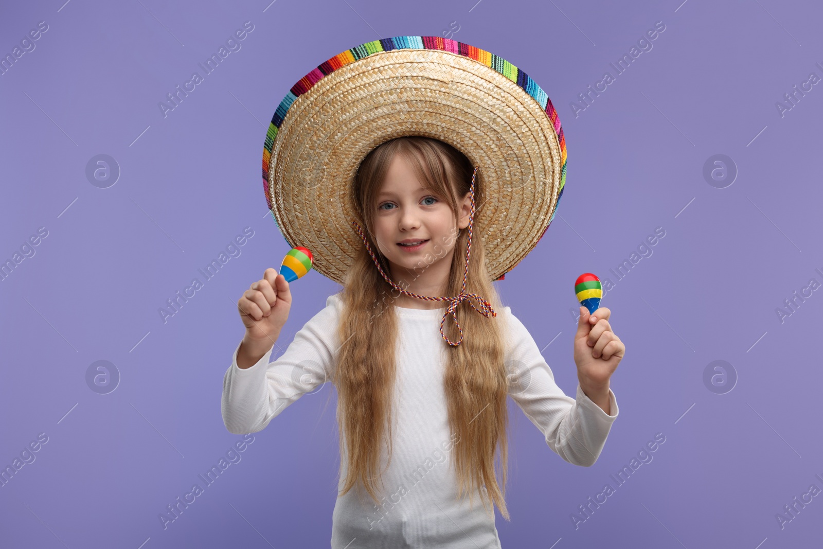 Photo of Cute girl in Mexican sombrero hat with maracas on purple background