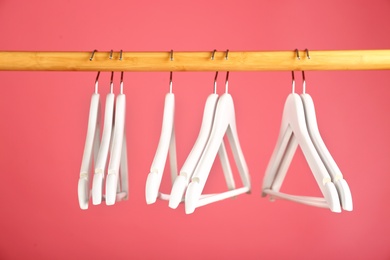 Photo of Empty clothes hangers on wooden rail against color background