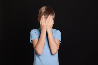 Boy covering face with hands on black background. Children's bullying
