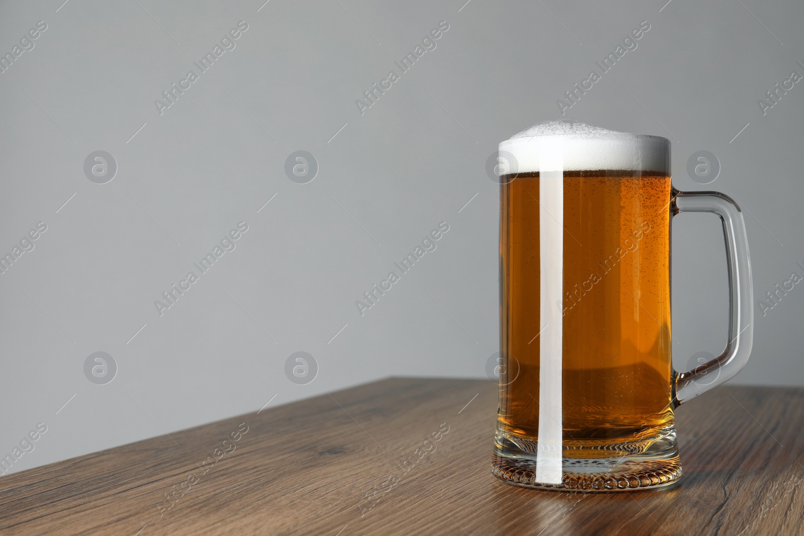 Photo of Glass mug of tasty dark beer on wooden table against grey background. Space for text