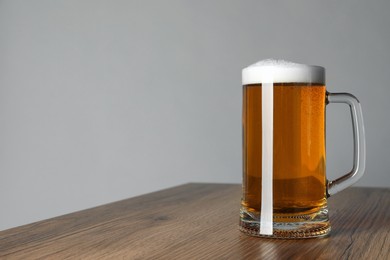Glass mug of tasty dark beer on wooden table against grey background. Space for text