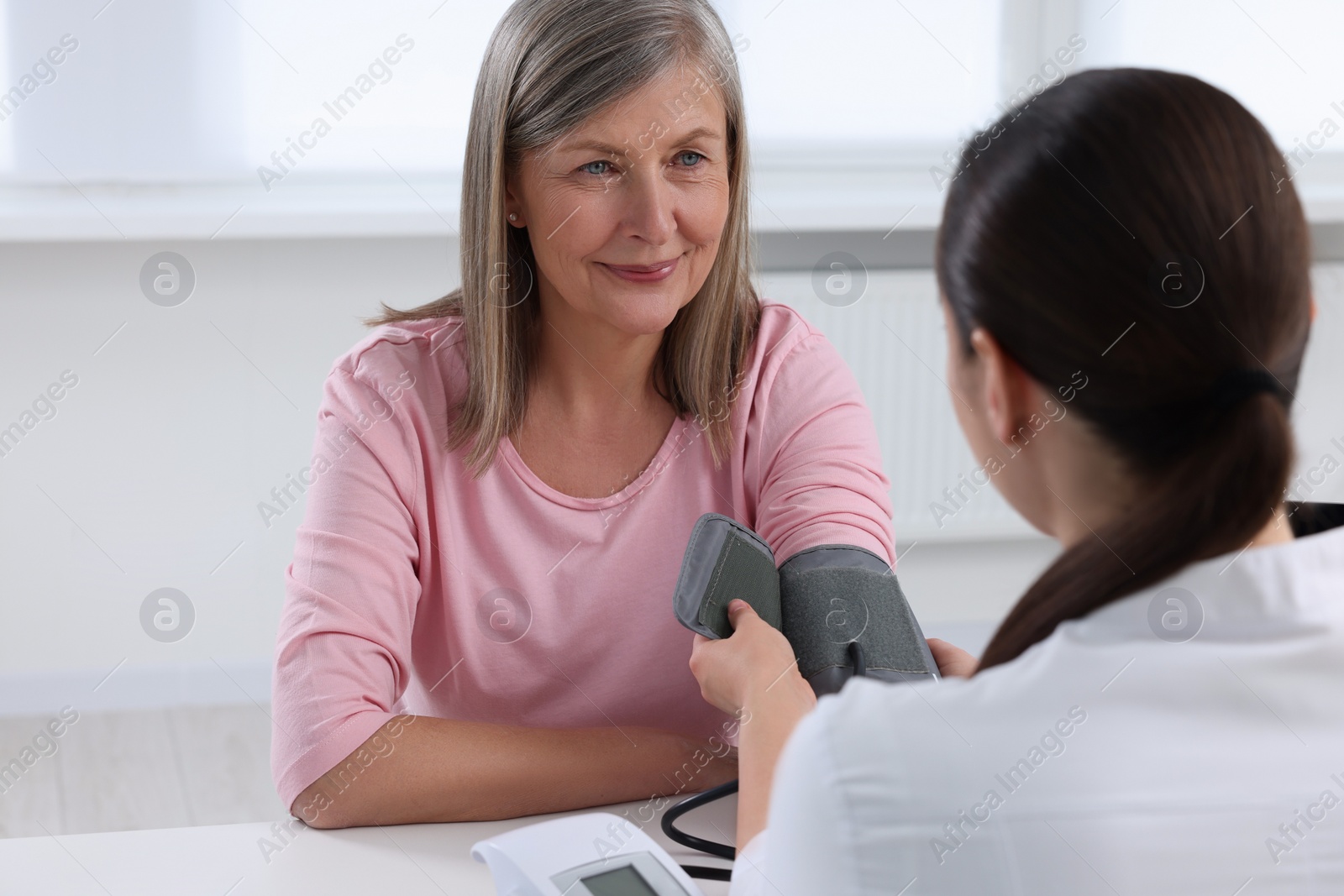 Photo of Doctor measuring blood pressure of woman at table indoors