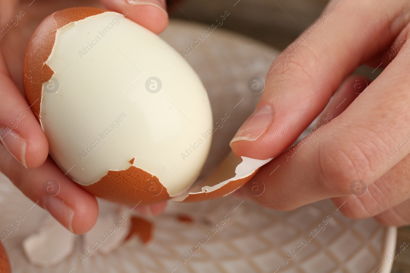 Photo of Woman peeling boiled egg over plate, closeup