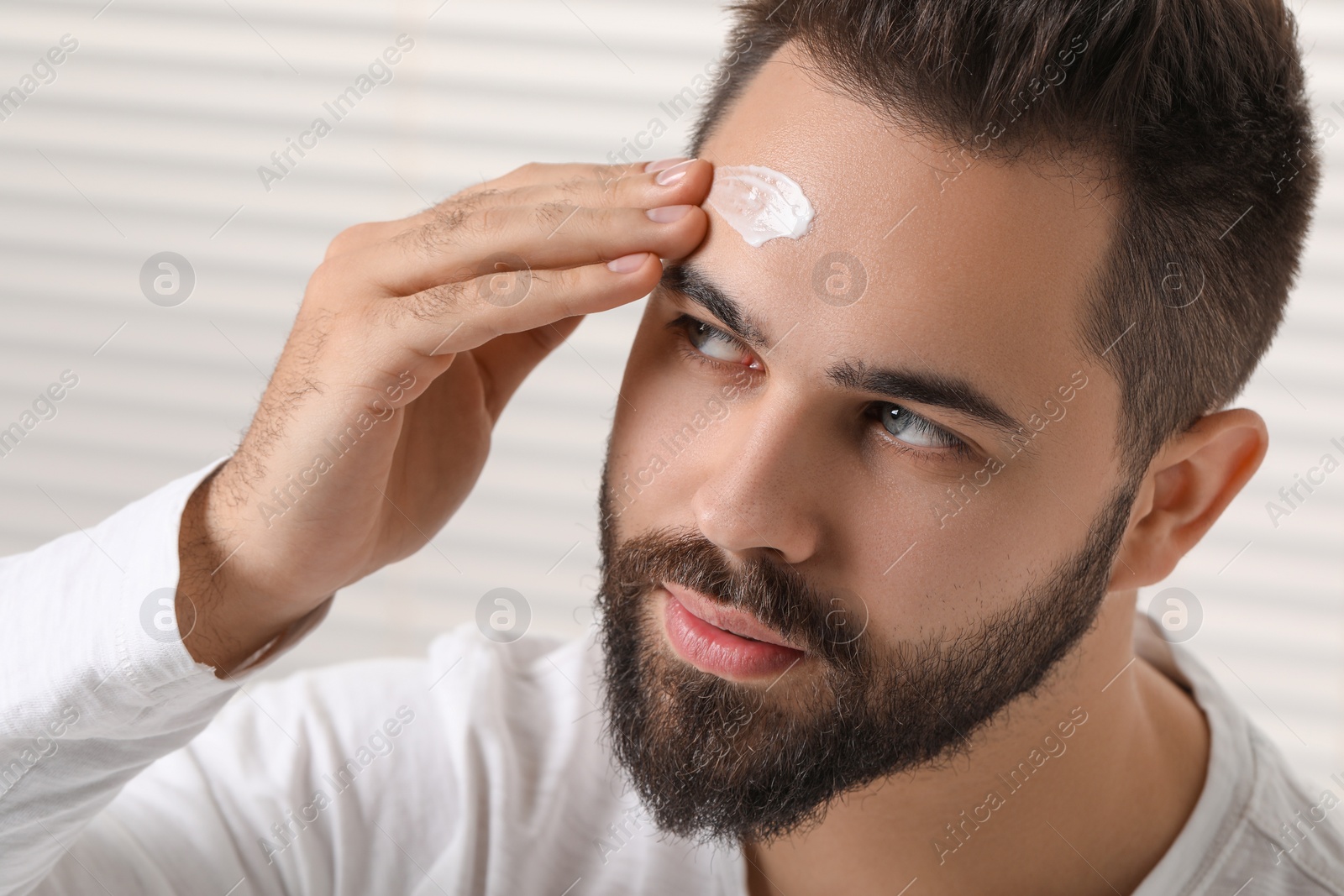 Photo of Man with dry skin applying cream onto his forehead indoors