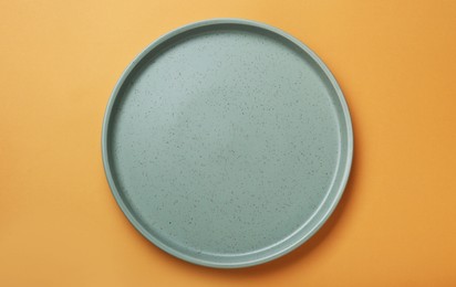 Empty ceramic plate on pale orange background, top view