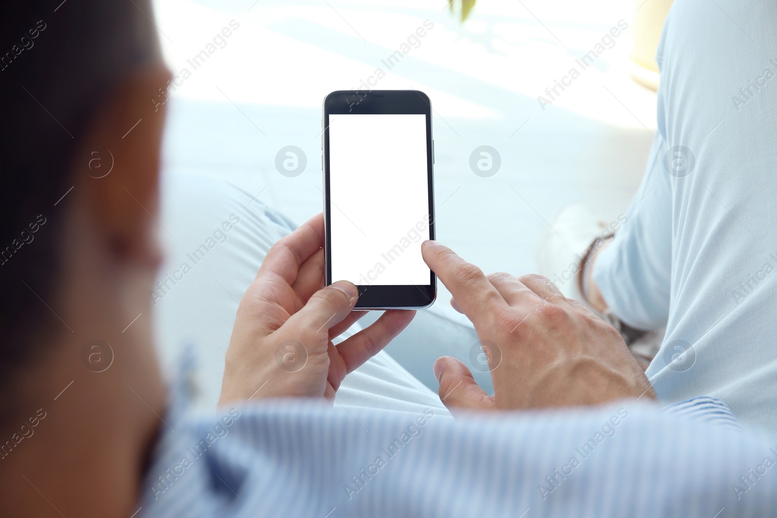 Photo of Young man holding mobile phone with blank screen in hand, indoors