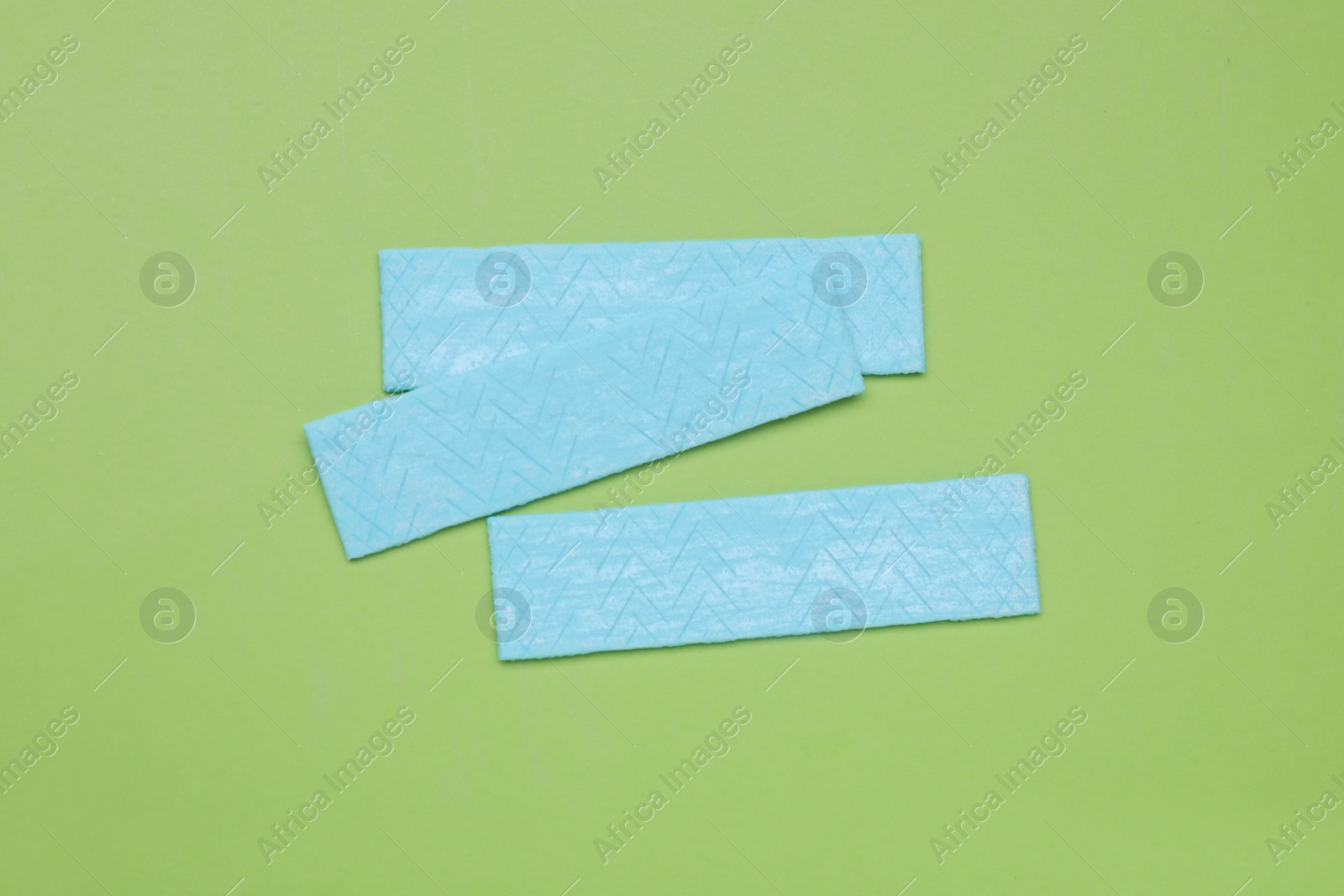 Photo of Sticks of tasty chewing gum on light green background, flat lay