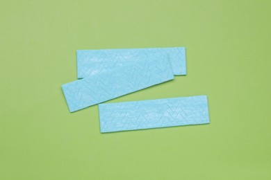 Sticks of tasty chewing gum on light green background, flat lay