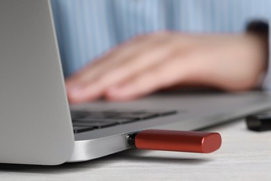 Photo of Woman using laptop with attached usb flash drive at wooden table, closeup