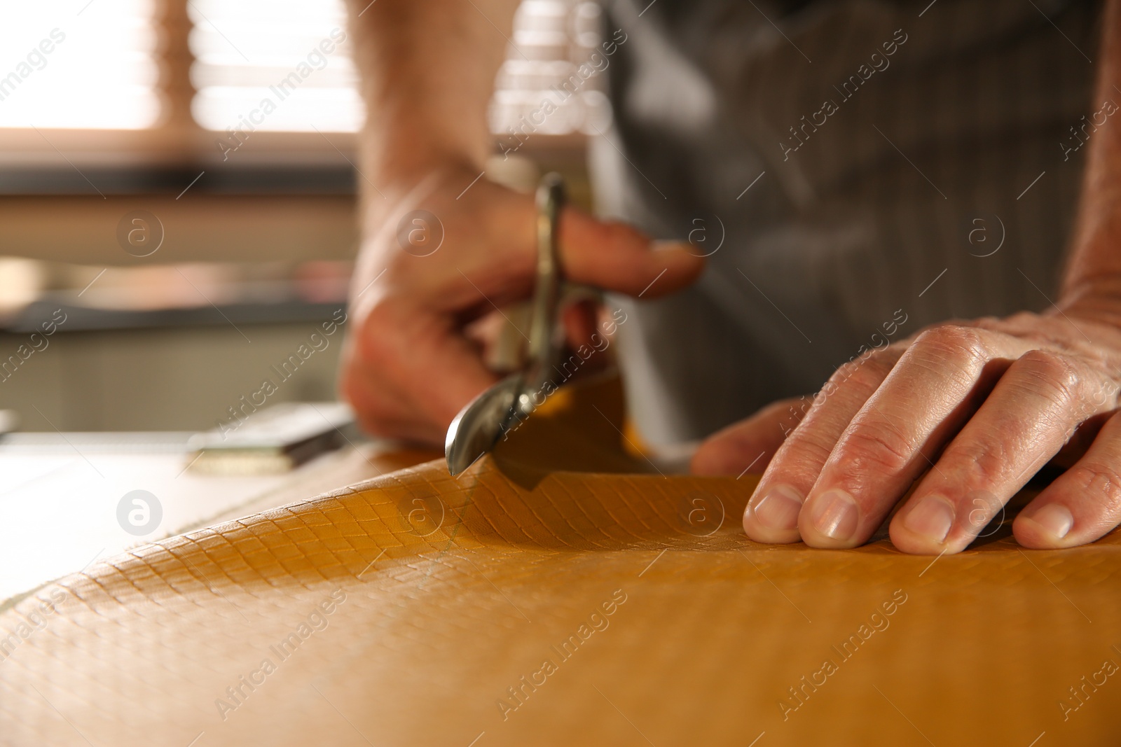 Photo of Man cutting leather with scissors in workshop, closeup