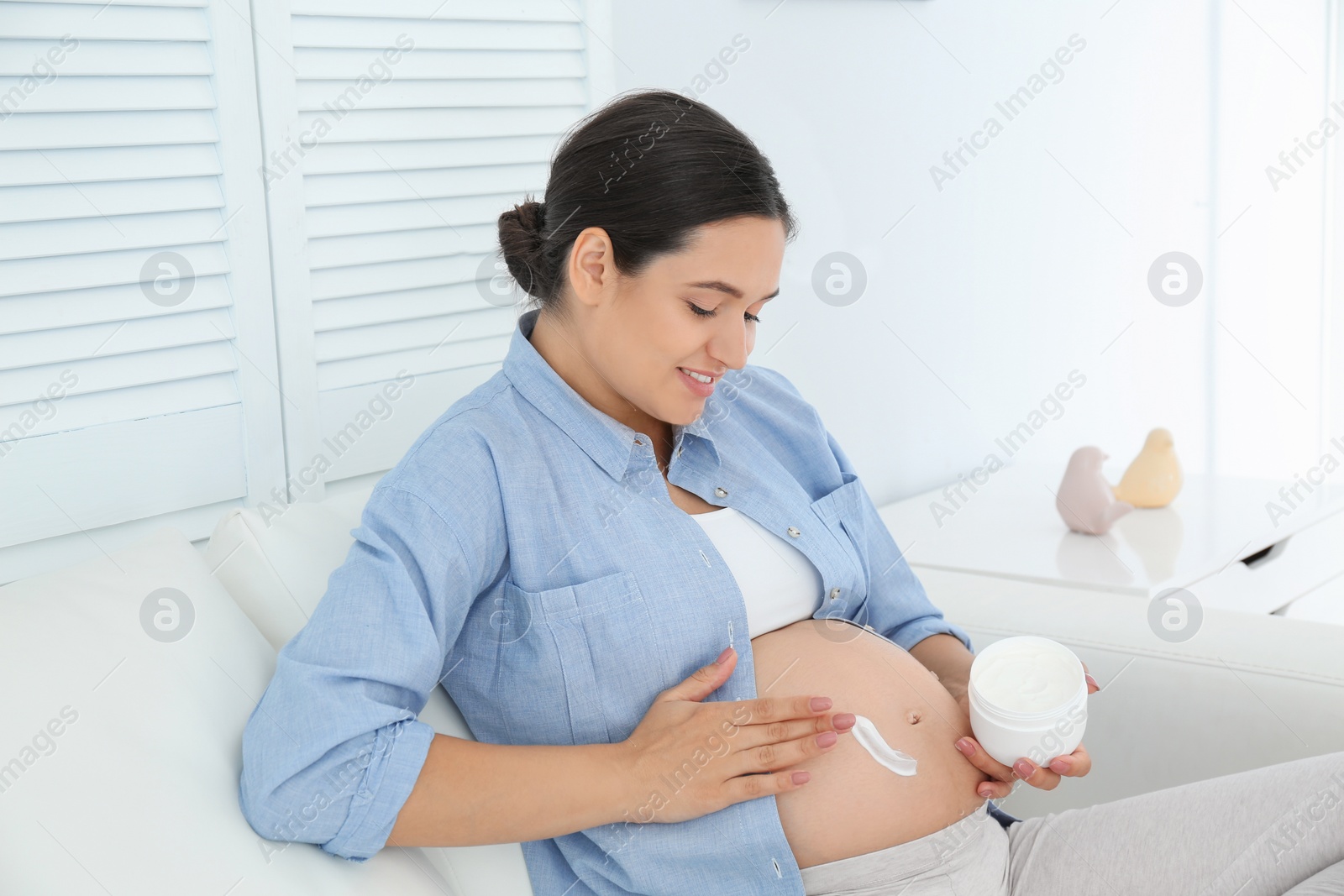 Photo of Pregnant woman applying body cream on belly at home