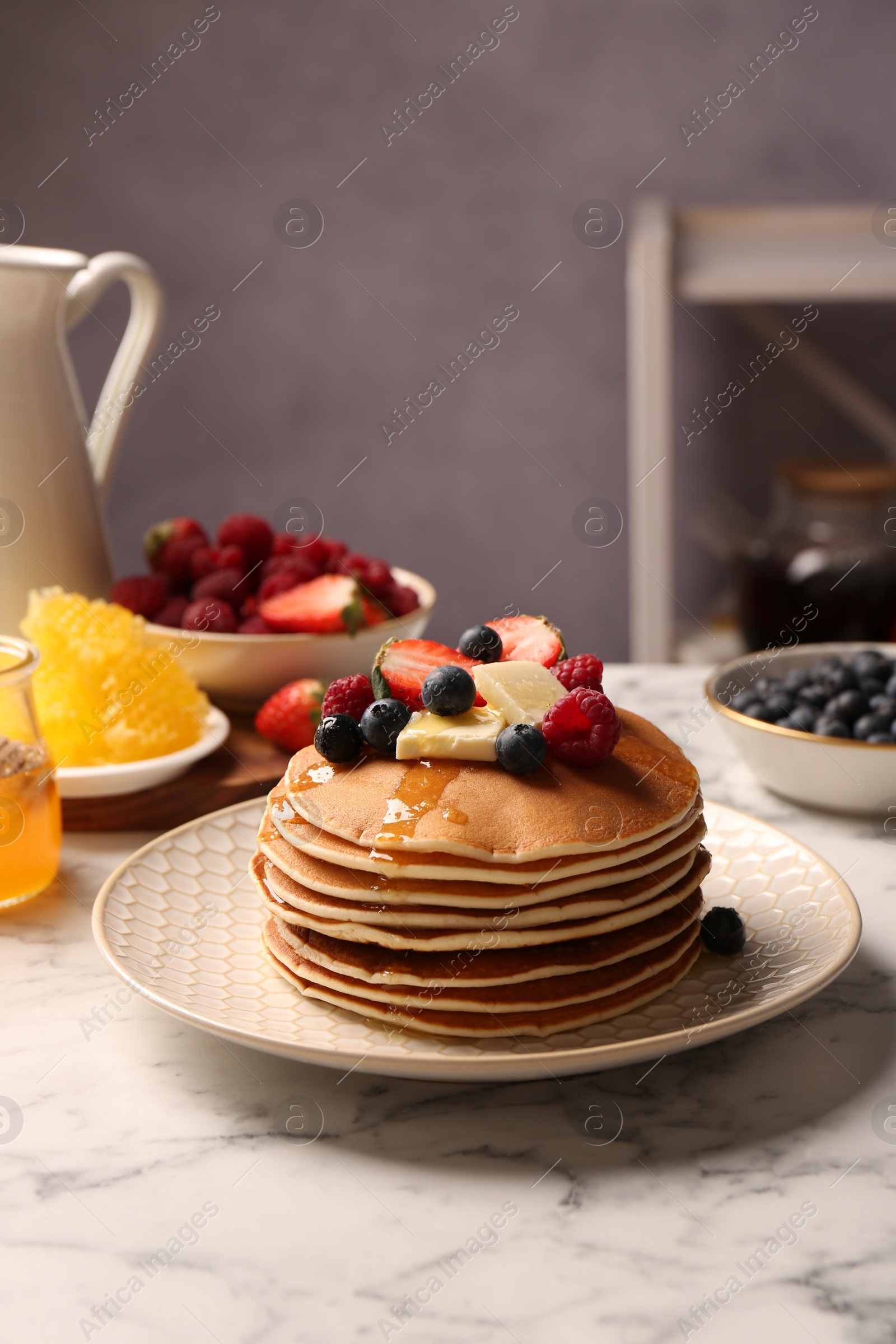 Photo of Delicious pancakes with fresh berries, butter and honey on white marble table, space for text