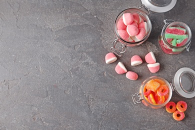 Photo of Flat lay composition with jars of tasty jelly candies on grey table, space for text