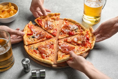 Photo of Young people taking slices of tasty pizza with meat at table