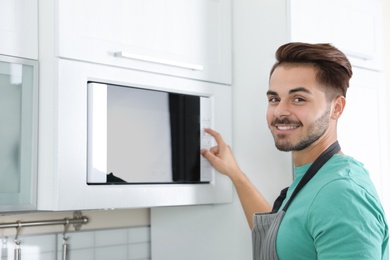 Photo of Young man using modern microwave oven at home