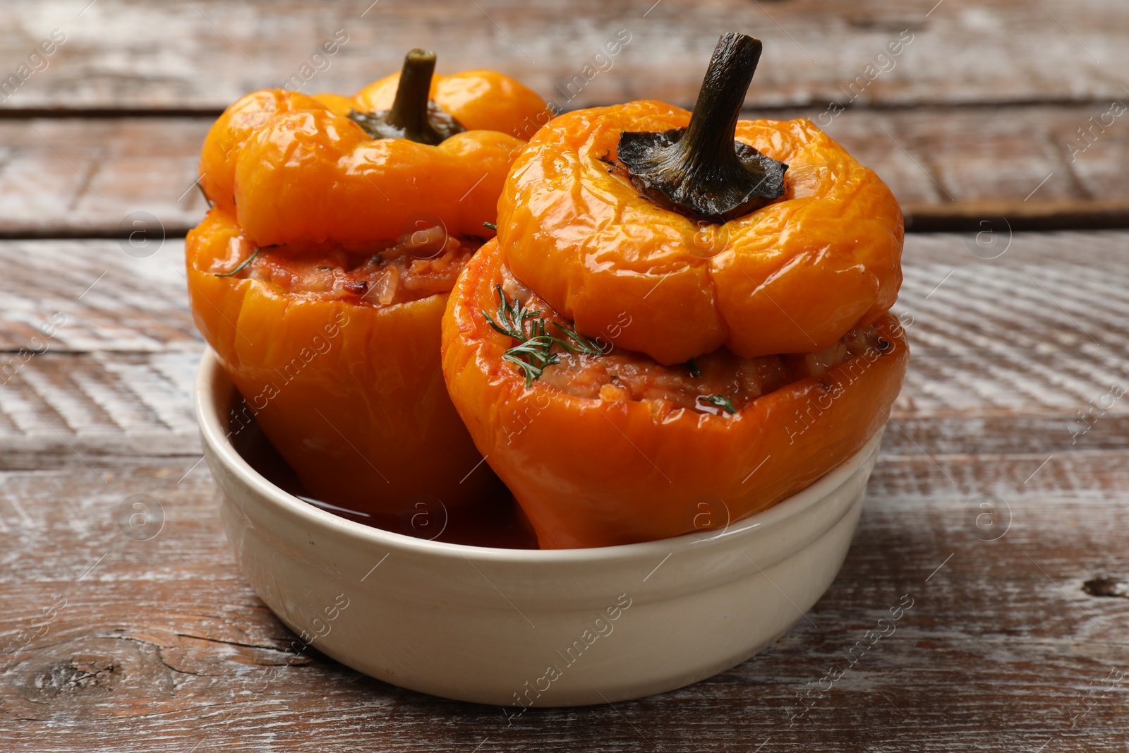 Photo of Tasty stuffed peppers in bowl on wooden rustic table, closeup