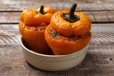 Photo of Tasty stuffed peppers in bowl on wooden rustic table, closeup