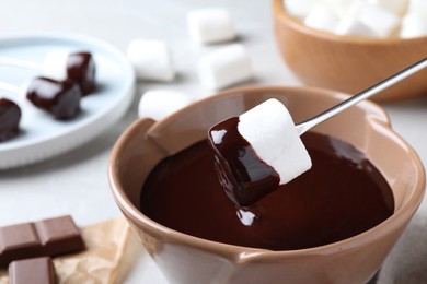 Photo of Dipping marshmallow into melted dark chocolate, closeup