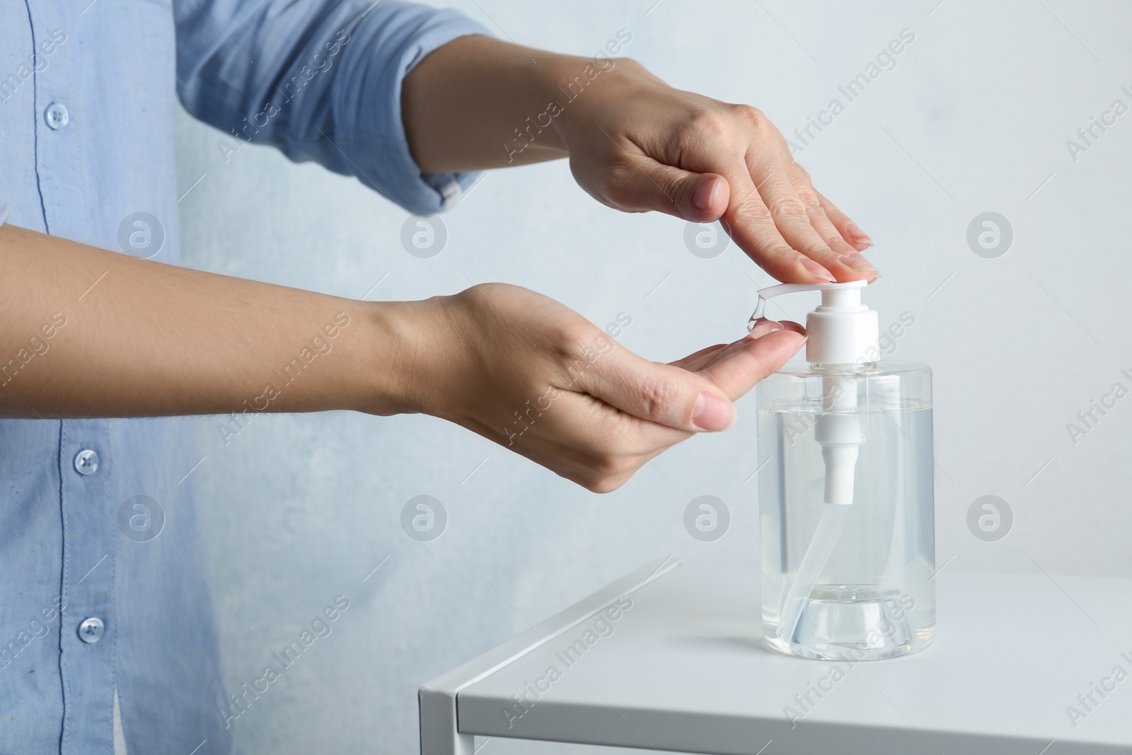 Photo of Woman applying antiseptic gel onto hand at table against light background, closeup. Virus prevention