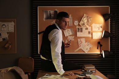 Photo of Old fashioned detective with drink near investigation board in office