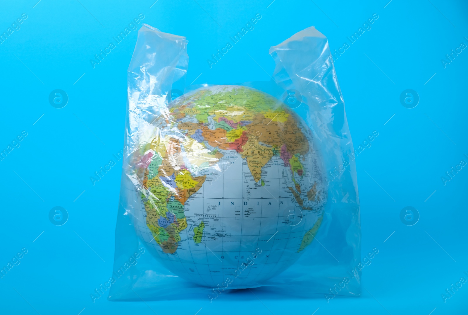 Photo of Globe in plastic bag on turquoise background. Environmental conservation