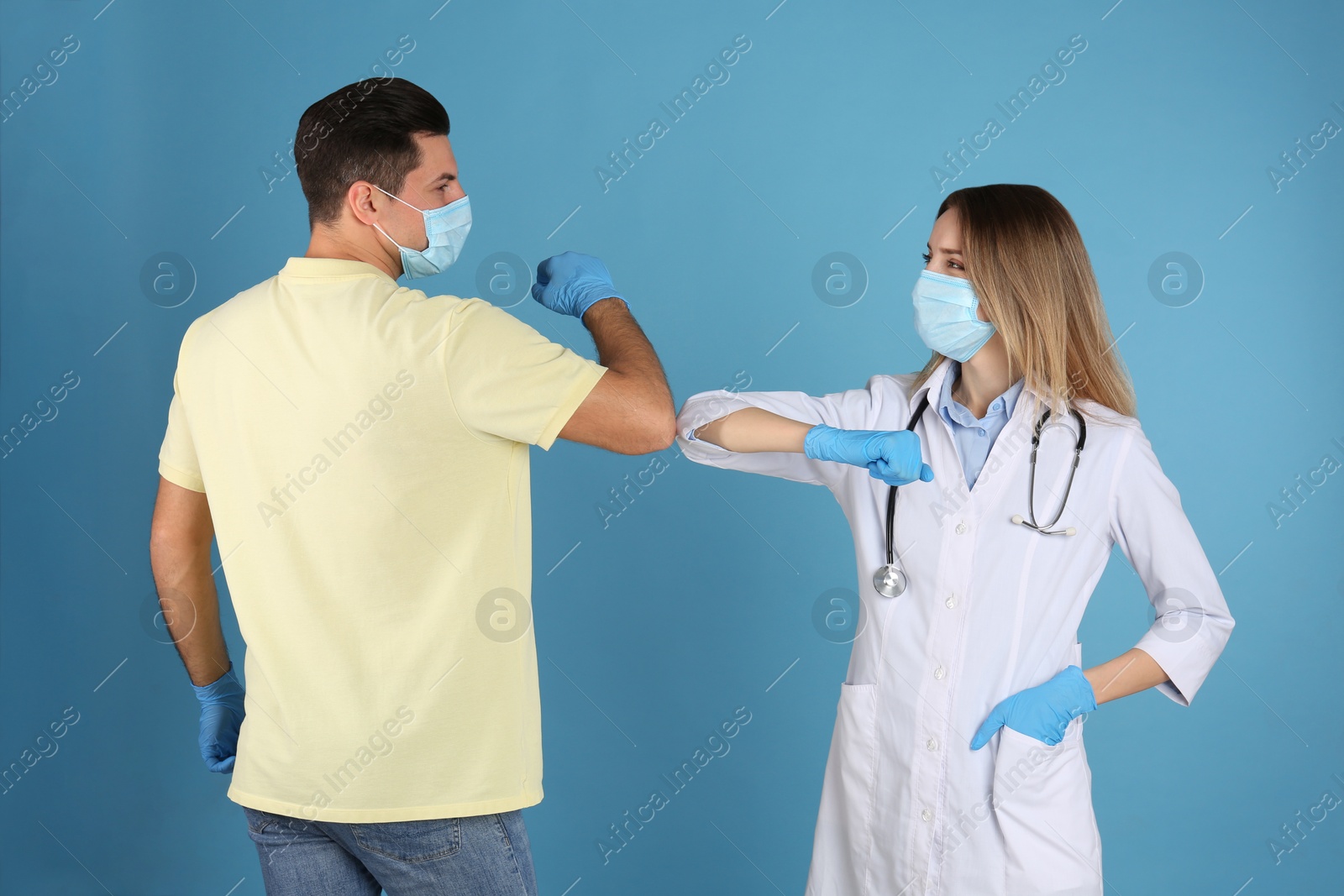 Photo of Doctor and patient doing elbow bump instead of handshake on light blue background. New greeting during COVID-19 pandemic
