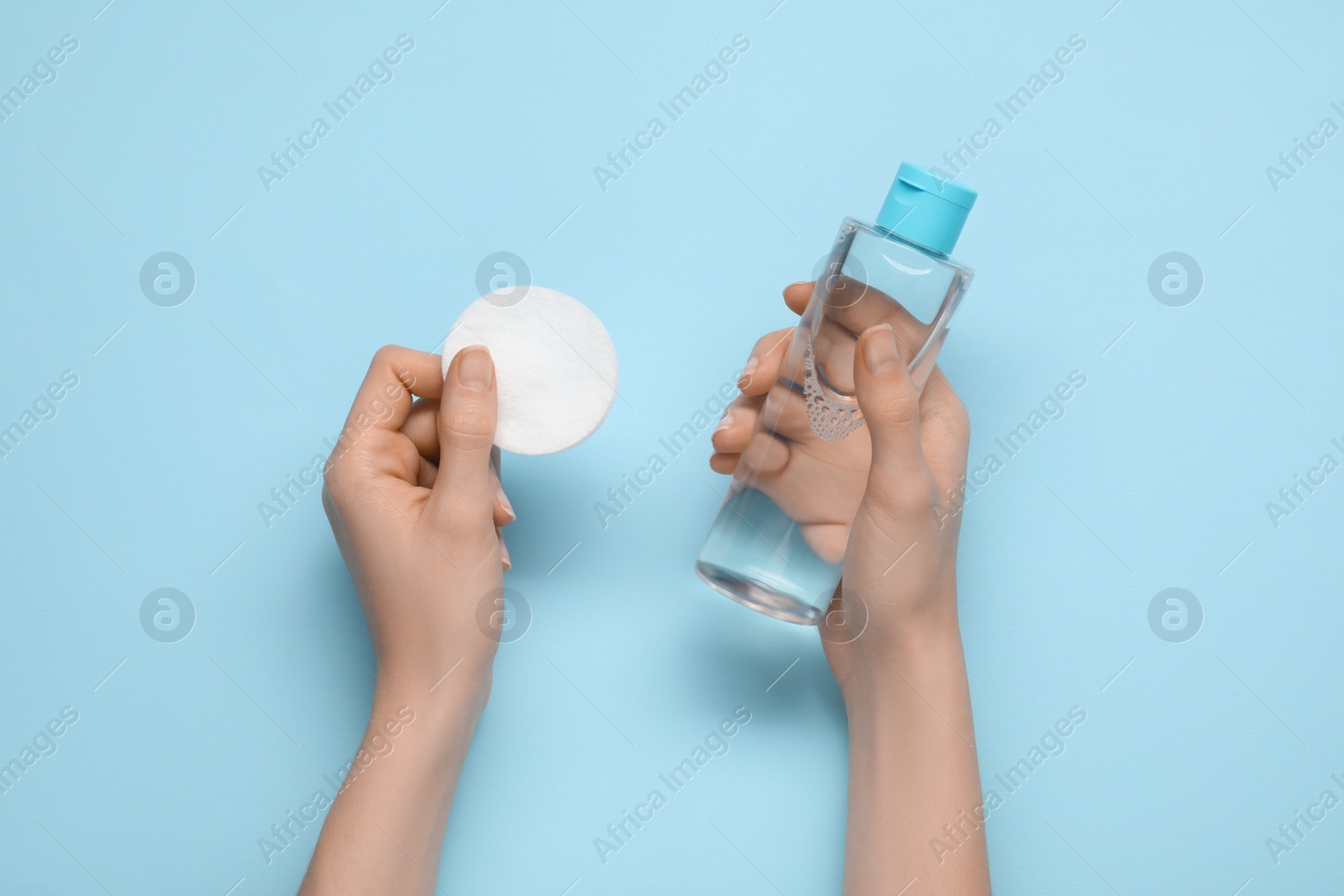 Photo of Woman holding makeup remover and cotton pad on light blue background, top view