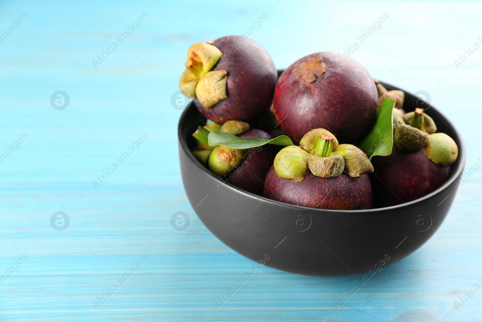 Photo of Fresh ripe mangosteen fruits on light blue wooden table. Space for text