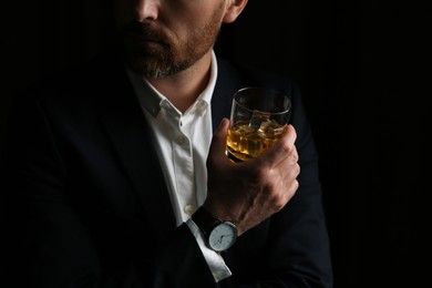 Photo of Man holding glass of whiskey with ice cubes on black background, closeup. Space for text