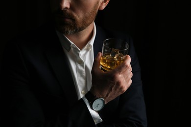 Man holding glass of whiskey with ice cubes on black background, closeup. Space for text