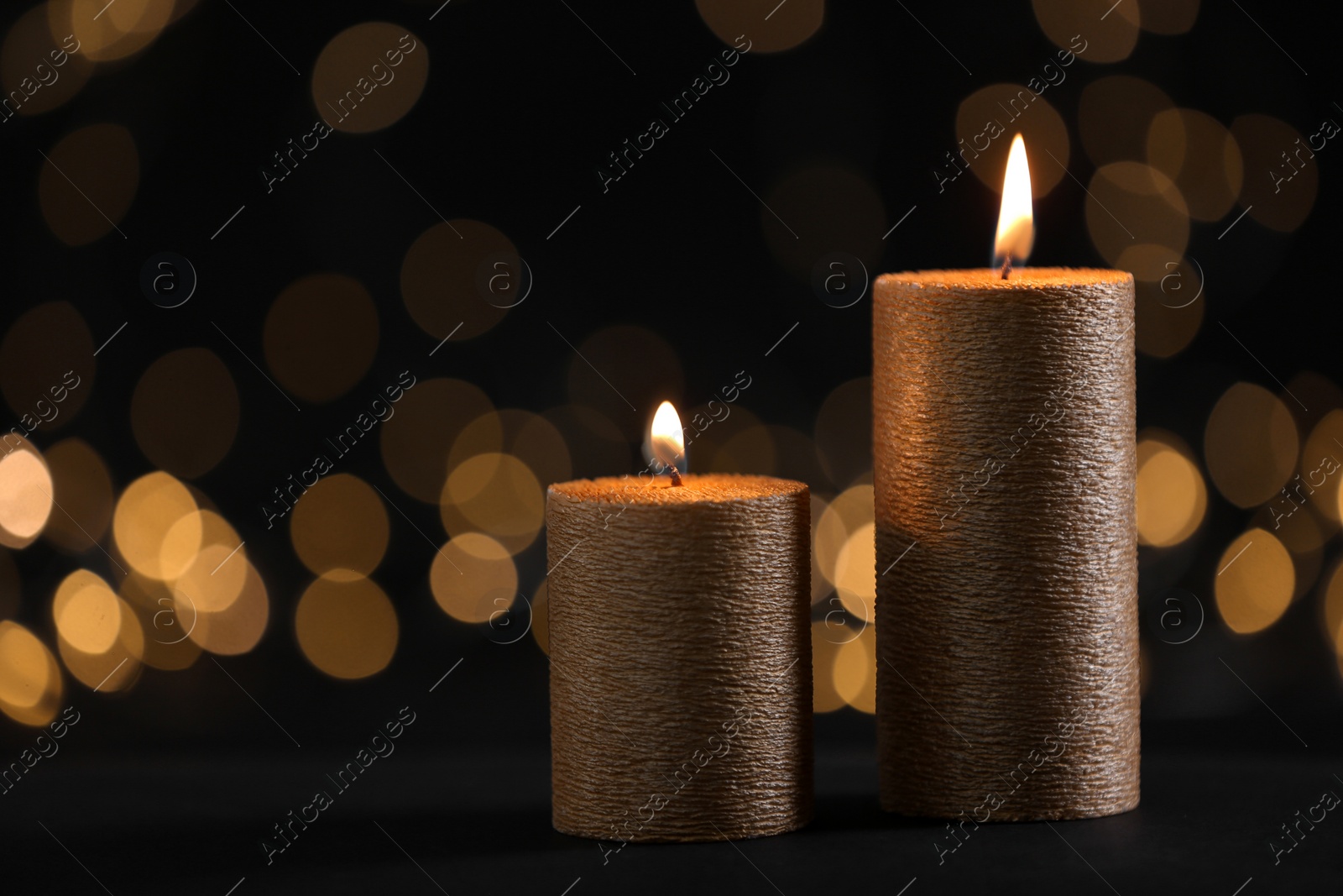 Photo of Burning gold candles against blurred lights in darkness. Space for text