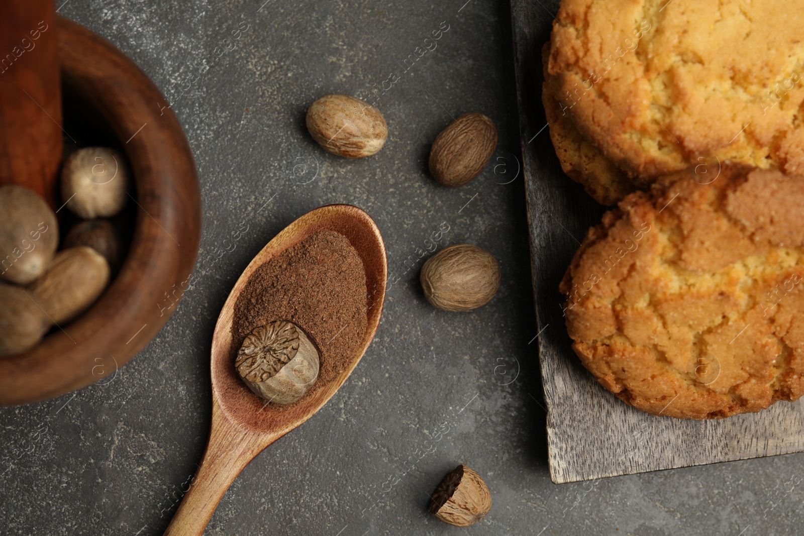 Photo of Nutmeg powder, seeds and cookies on grey table, flat lay