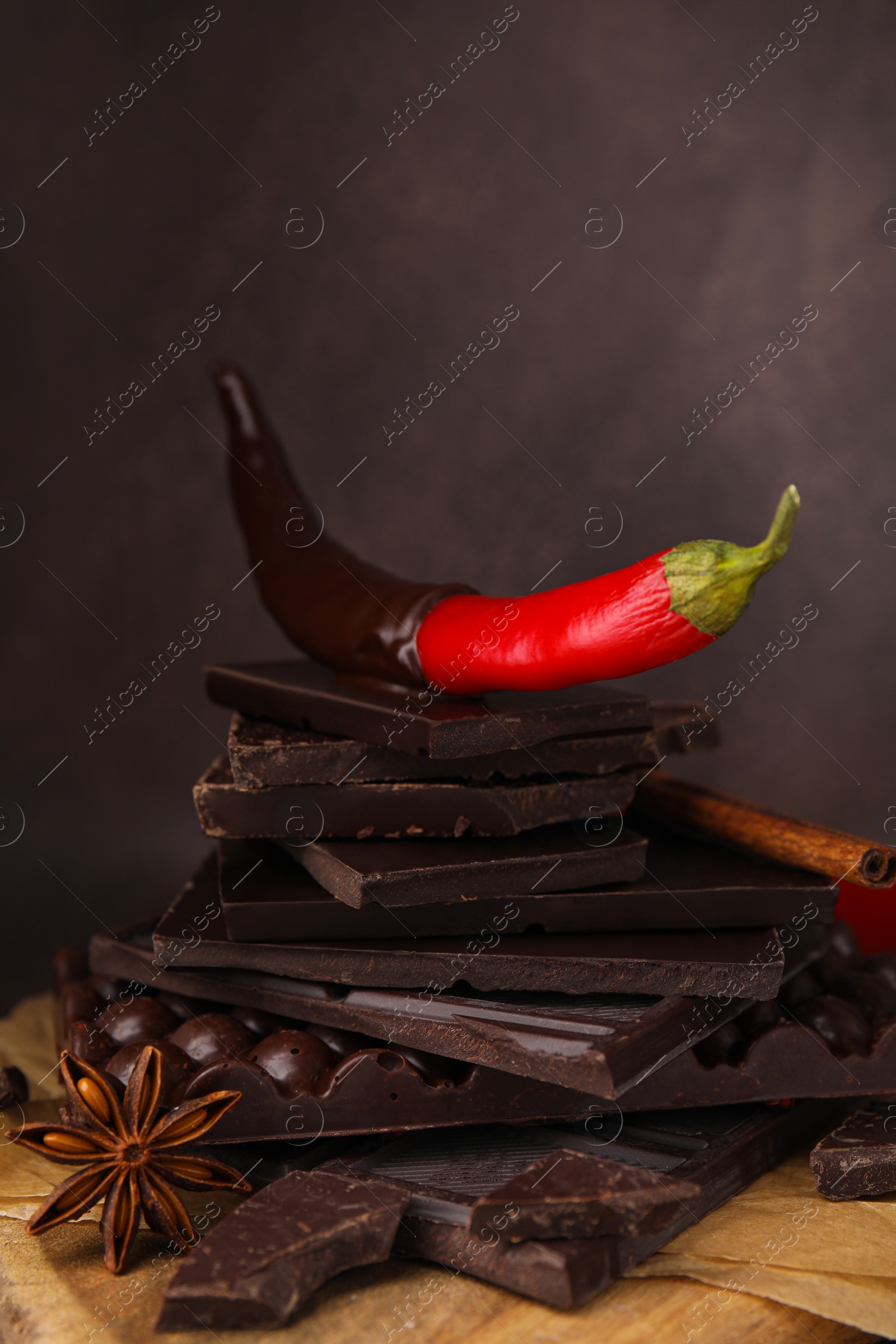 Photo of Red hot chili pepper and pieces of dark chocolate with spices on wooden board, closeup