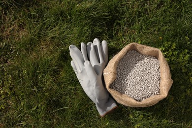 Photo of Fertilizer in bag and gloves on green grass outdoors, flat lay. Space for text