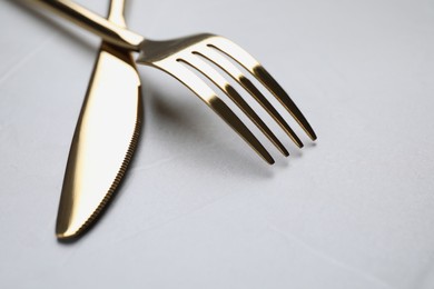 Photo of Golden fork and knife on light grey table, closeup. Space for text