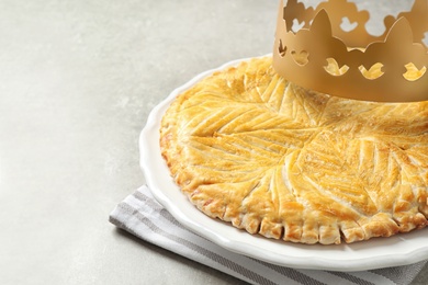 Traditional galette des Rois with paper crown on light grey table, closeup