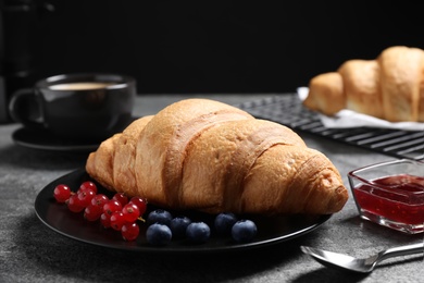 Plate with fresh crispy croissant and berries on grey table