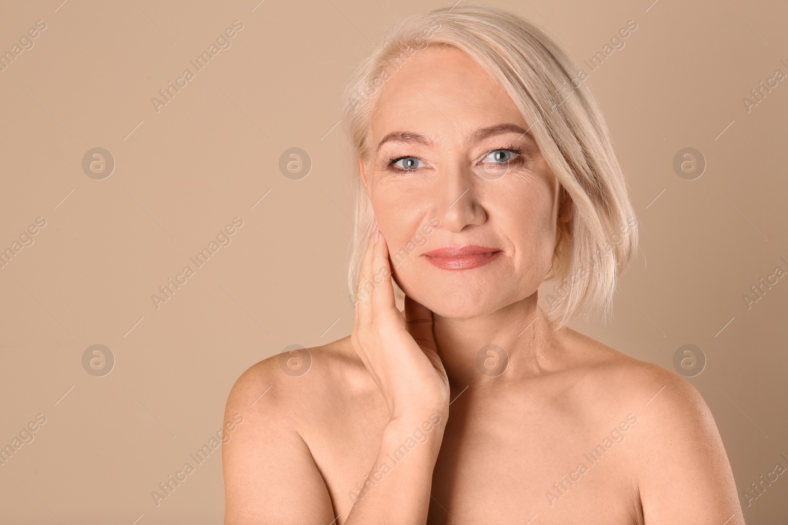 Photo of Portrait of charming mature woman with healthy beautiful face skin and natural makeup on beige background, space for text