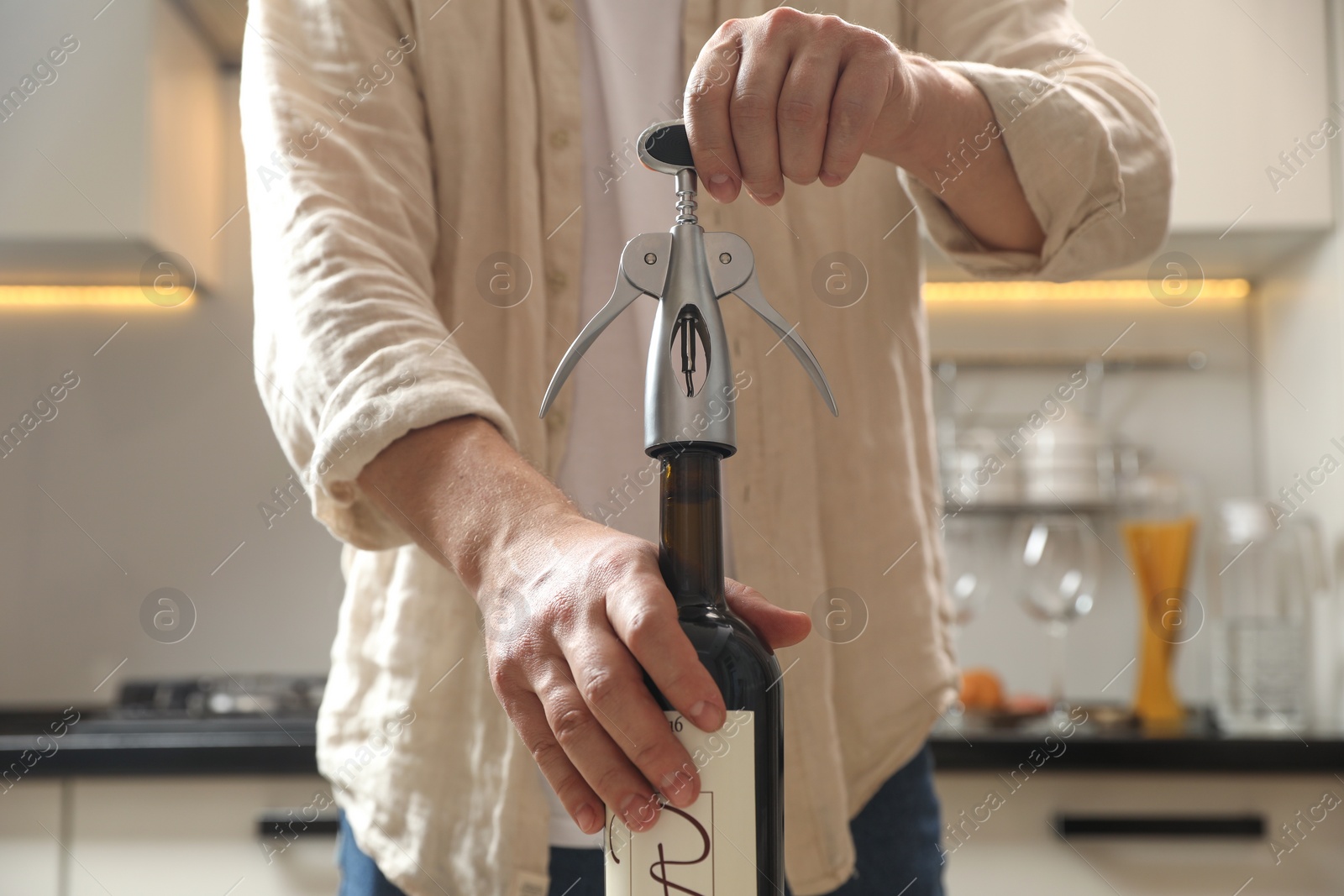 Photo of Man opening wine bottle with corkscrew in kitchen, closeup