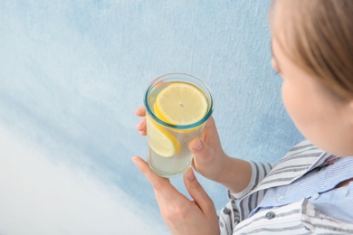 Young woman holding glass with lemon cocktail against color background