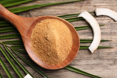 Photo of Spoon with coconut sugar, slices of fruit and palm leaves on wooden table, flat lay