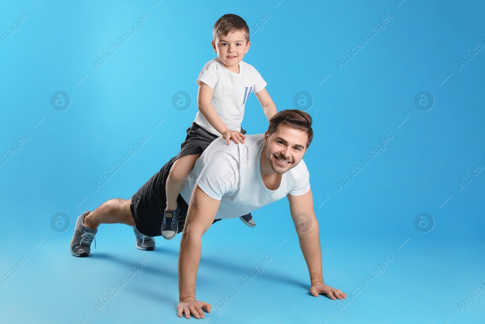 Photo of Dad doing push-ups with son on his back against color background