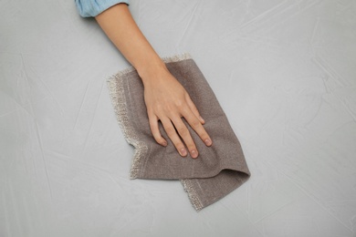 Woman wiping grey table with kitchen towel, top view