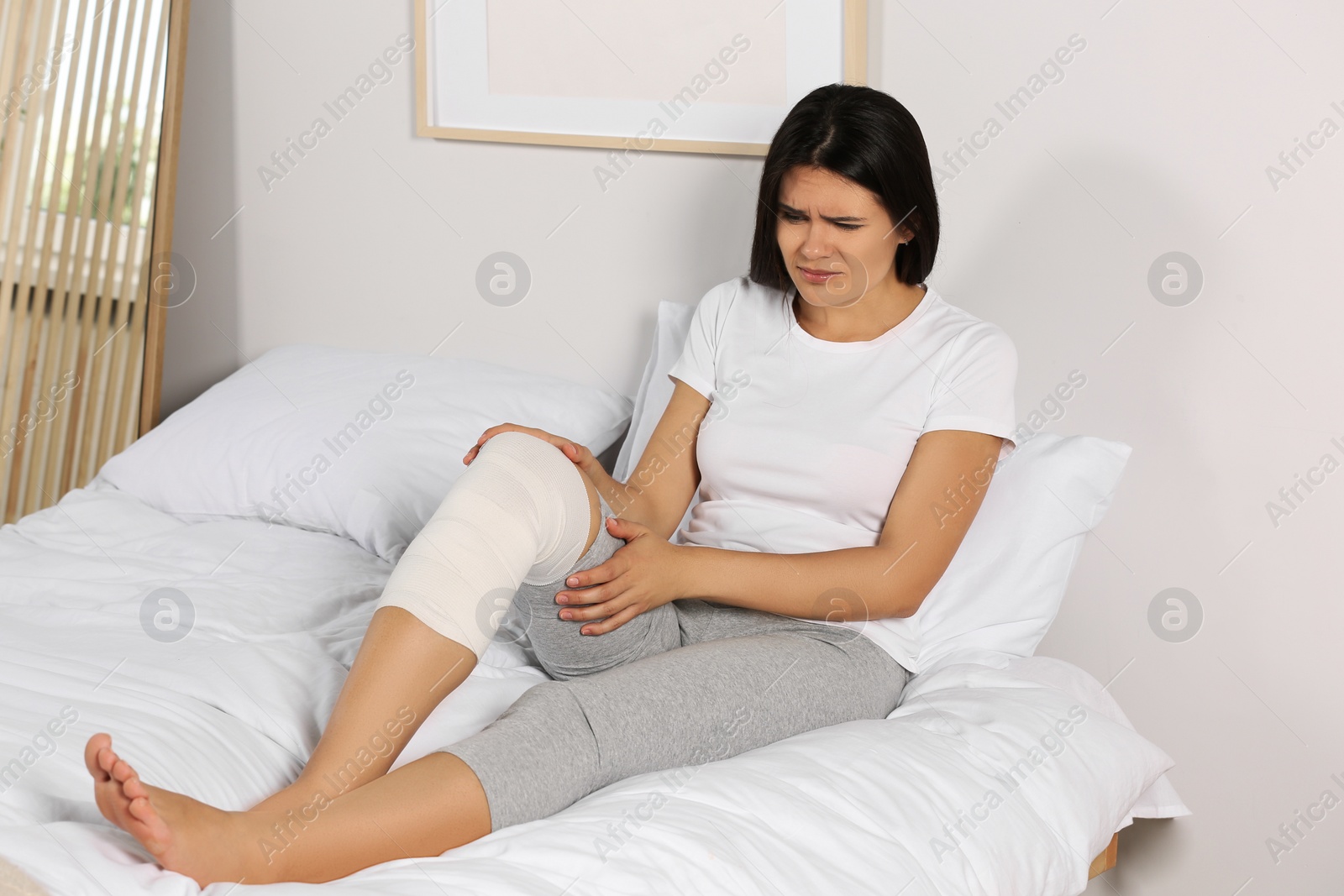 Photo of Young woman with leg wrapped in medical bandage in bedroom