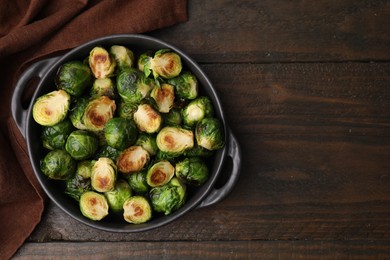 Photo of Delicious roasted Brussels sprouts in baking dish on wooden table, top view. Space for text